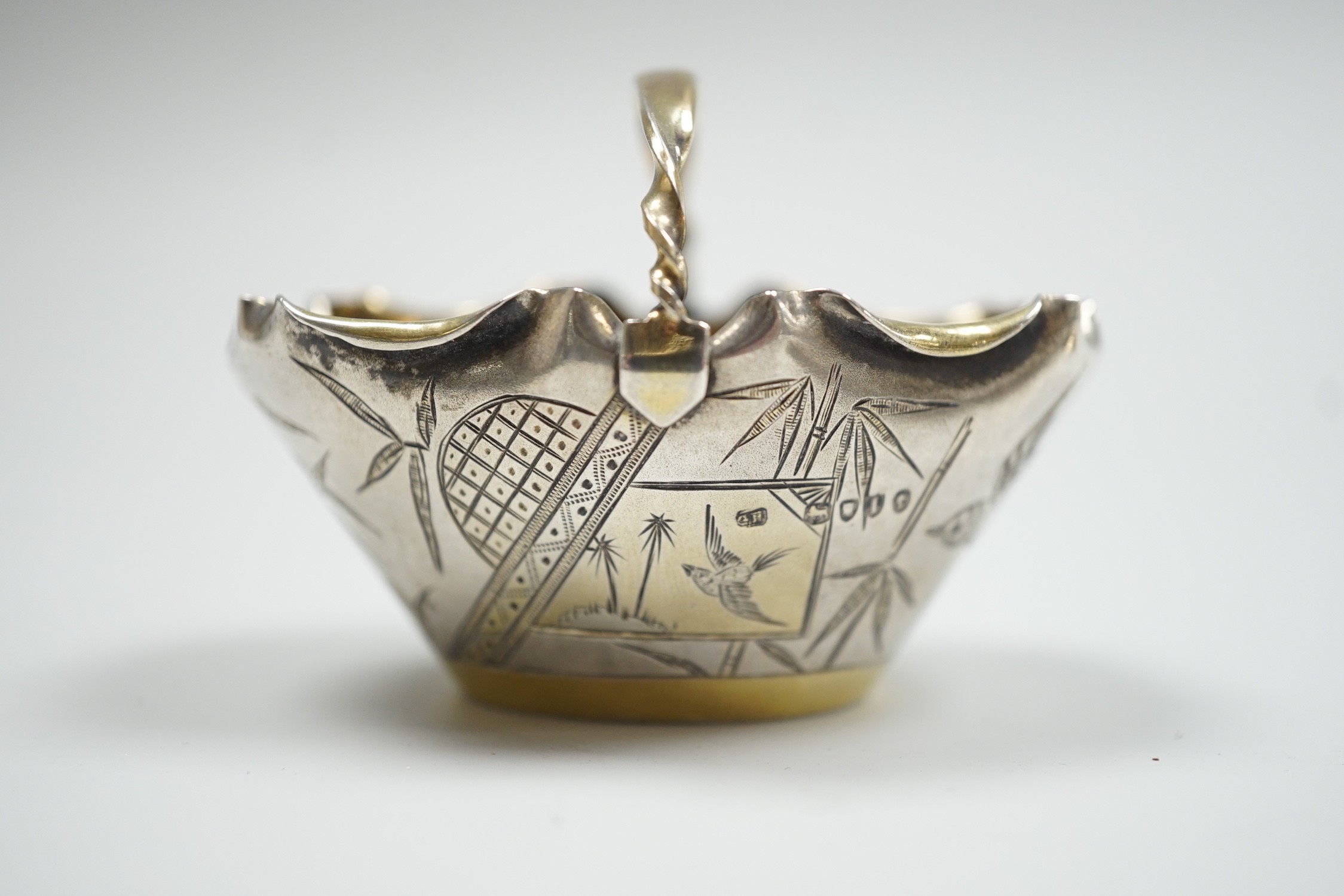 A late Victorian novelty parcel gilt silver salt modelled as a basket, with aesthetic engraved decoration, London, 1884, length 65mm, together with an Egyptian white metal small dish.